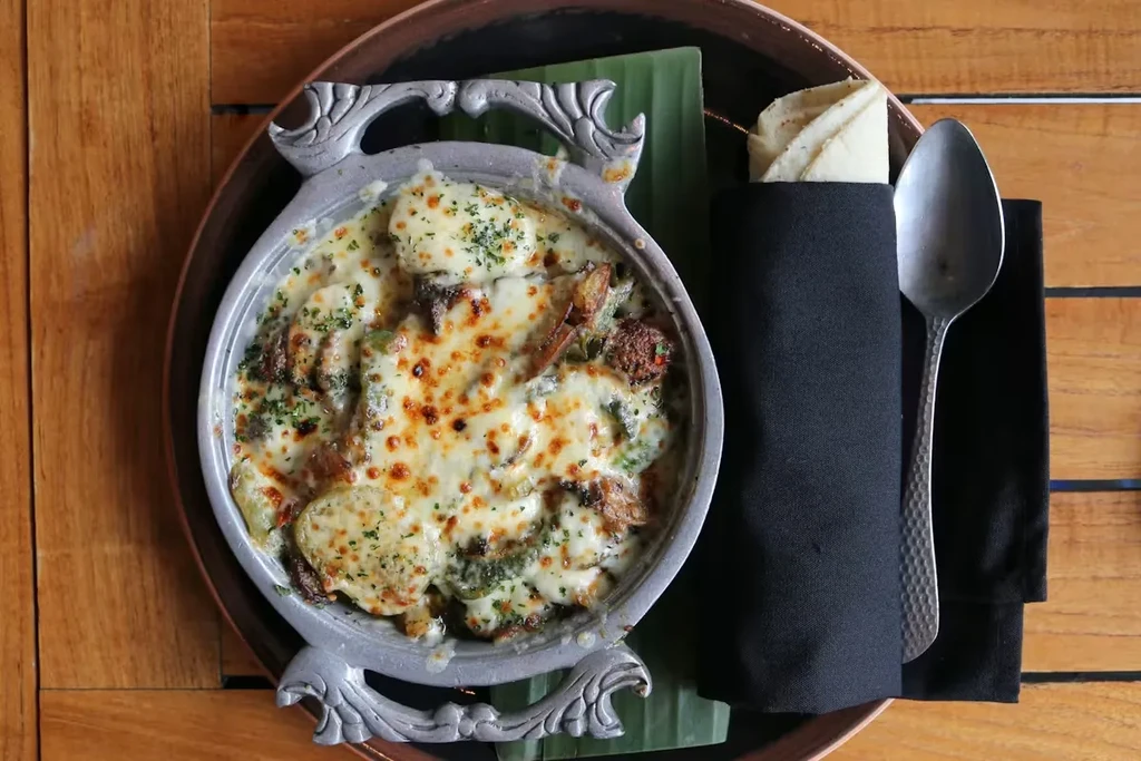 Overhead shot of a cheesy gratin or casserole in a silver bowl.