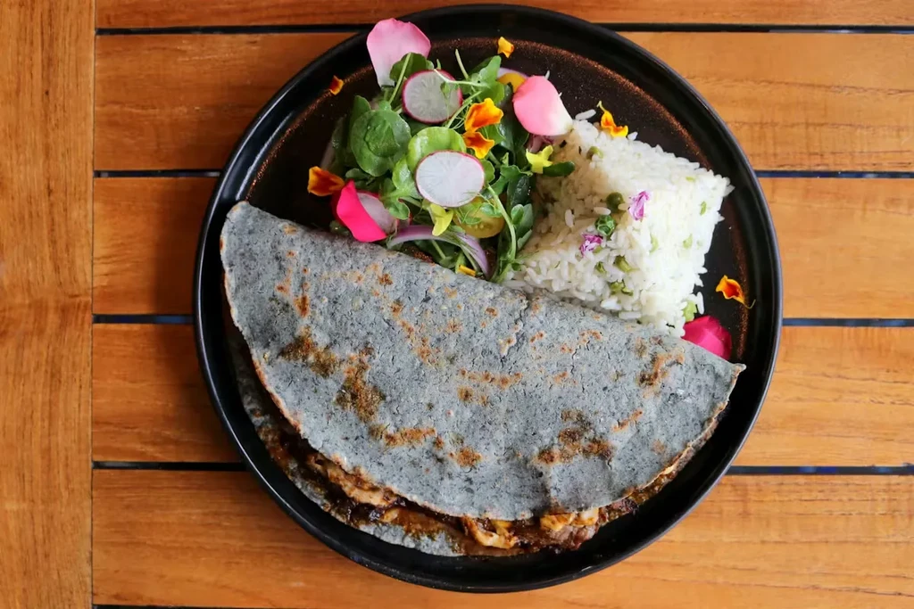 Blue corn quesadilla with rice and salad on a wooden table.