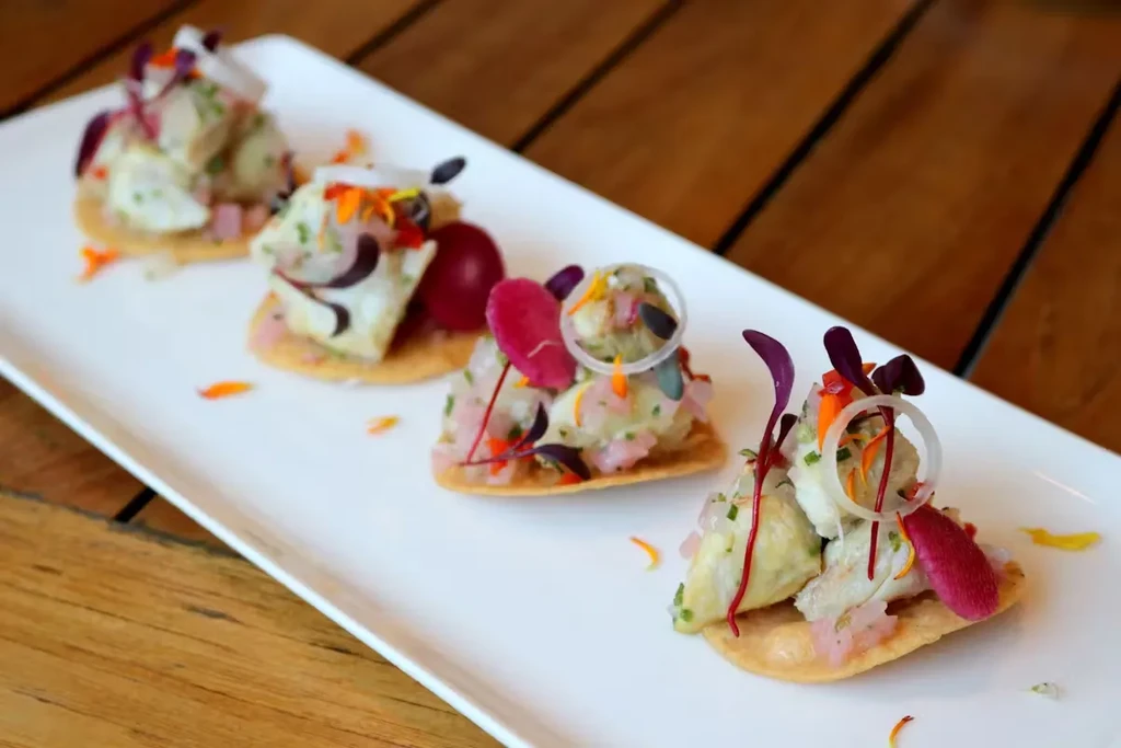 Four elegant ceviche tostadas on a rectangular white plate.