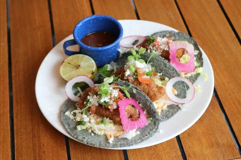 Overhead shot of three tacos with fish, cabbage, and microgreens.