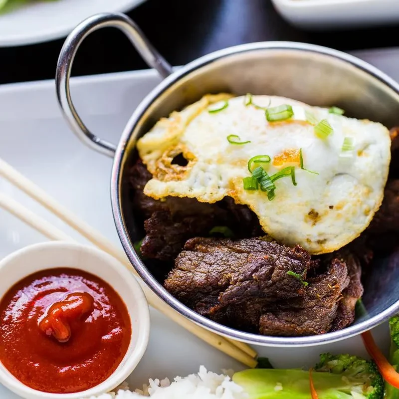 Beef and egg in a bowl with sauce, rice, and broccoli.