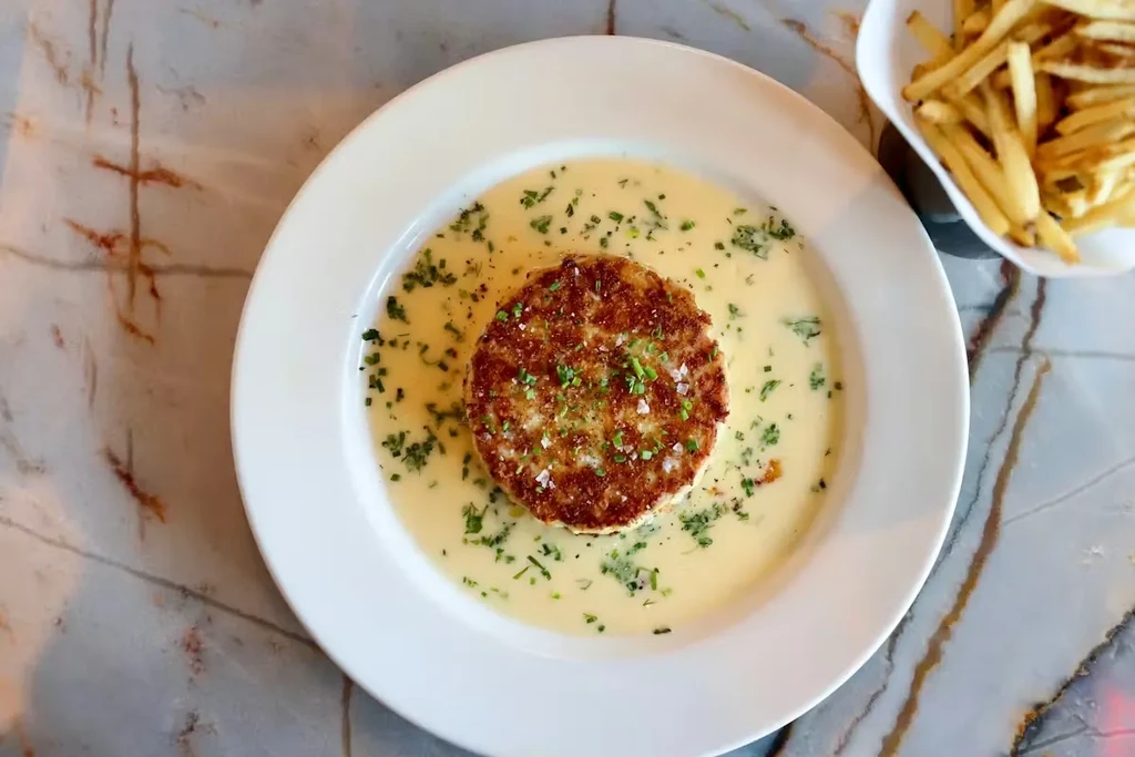 Fried patty with sauce, herbs, and french fries on a plate.
