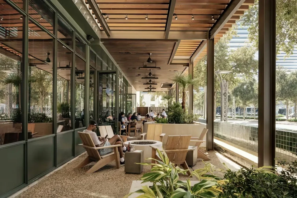 Outdoor restaurant patio with people, fire pit, tropical plants.