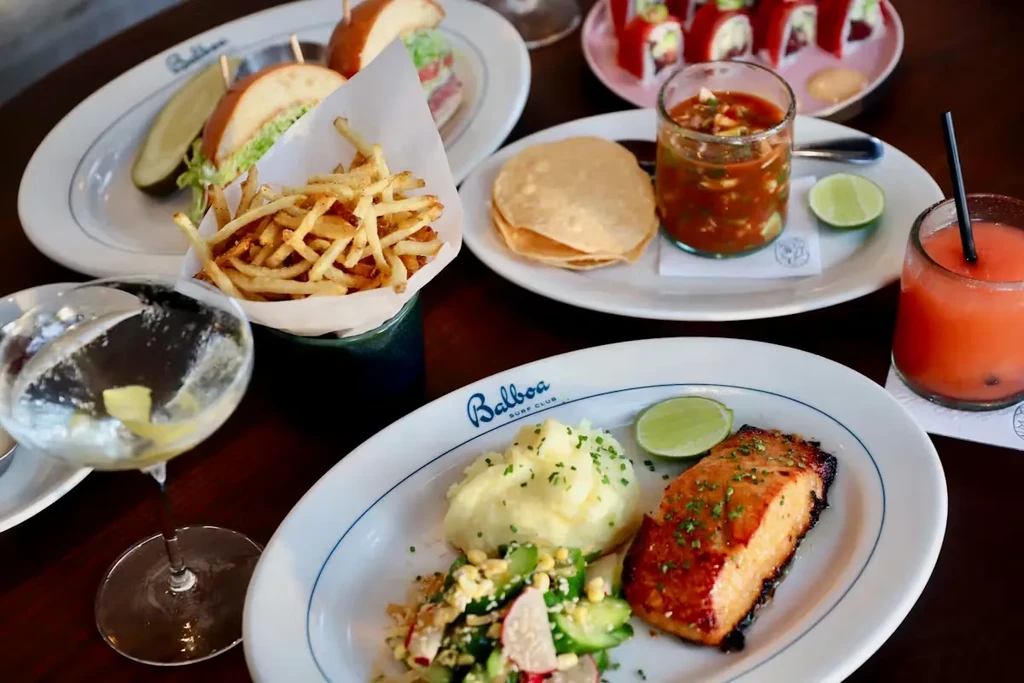 Table laden with grilled salmon, ceviche, sandwiches, and drinks.