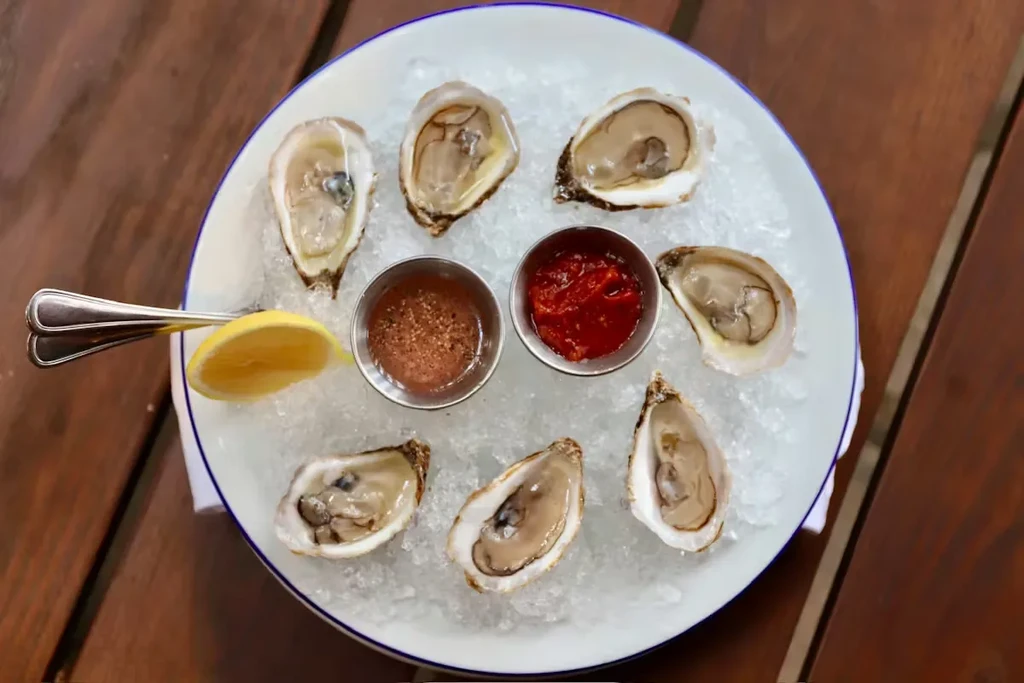 Seven fresh oysters on crushed ice with two sauces and a lemon.