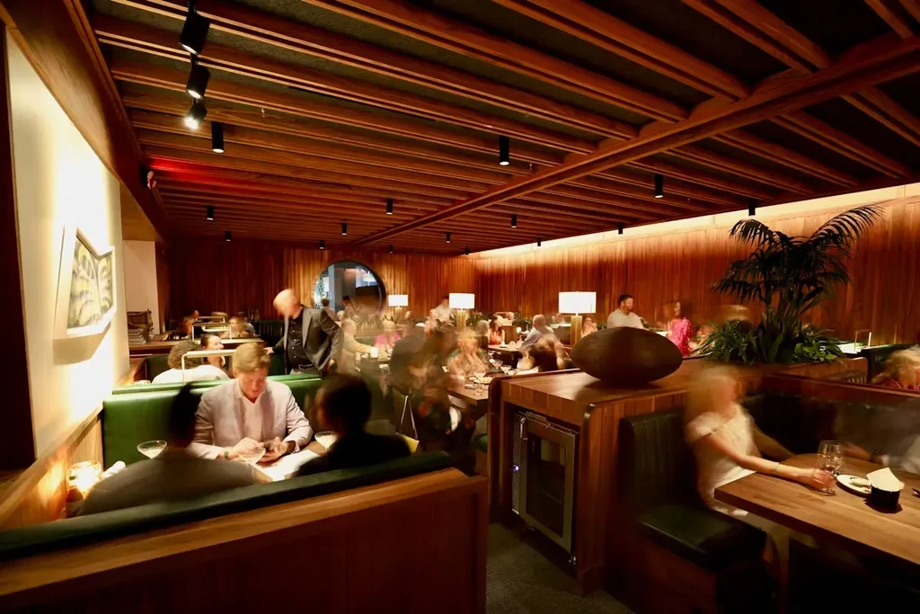 Warmly lit restaurant interior with dark wood paneling, booths, and patrons.