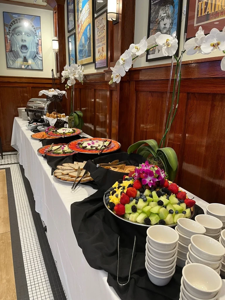 Buffet table with fruit platter, appetizers, bread, and orchid decorations.