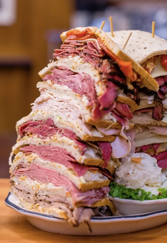 A very tall deli-style sandwich with meats, coleslaw, and potato salad.