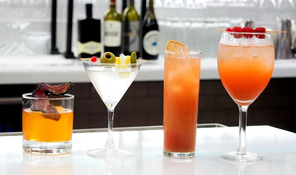 Four distinct cocktails, including one with bacon, on a white bar.