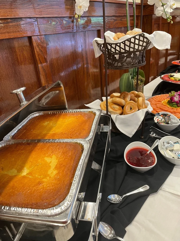 A buffet table laden with baked items, bagels, salmon, and jam.