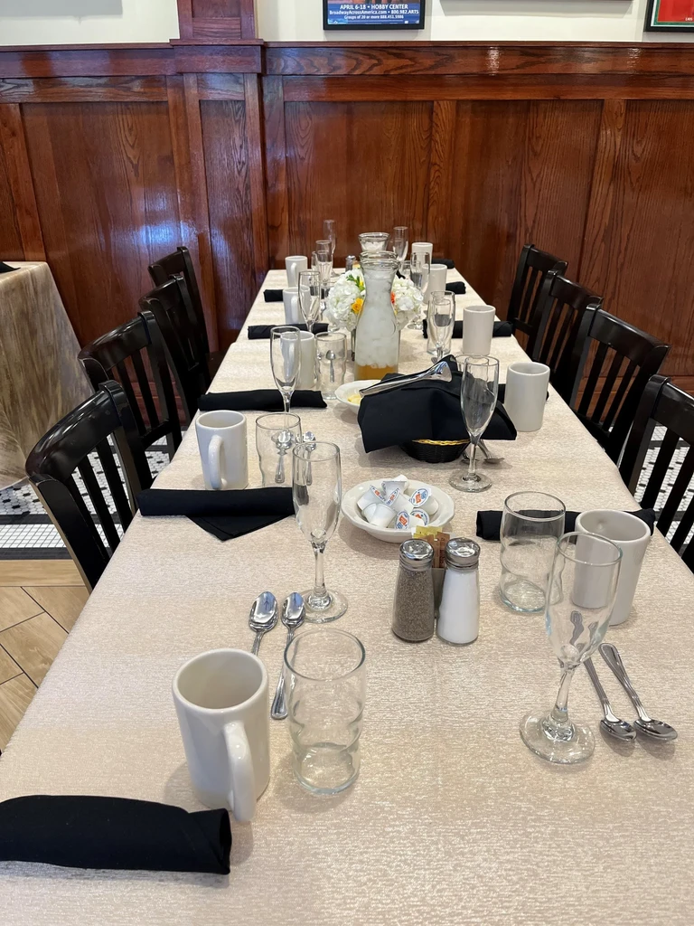 Long table set for dining with mugs, flutes, carafes.