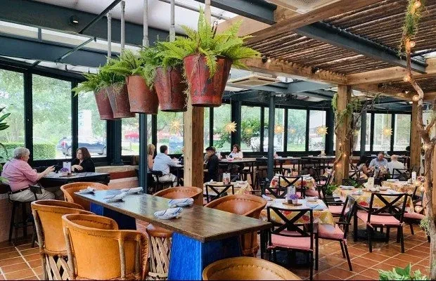 Restaurant interior with large windows, wooden structures, and patrons.