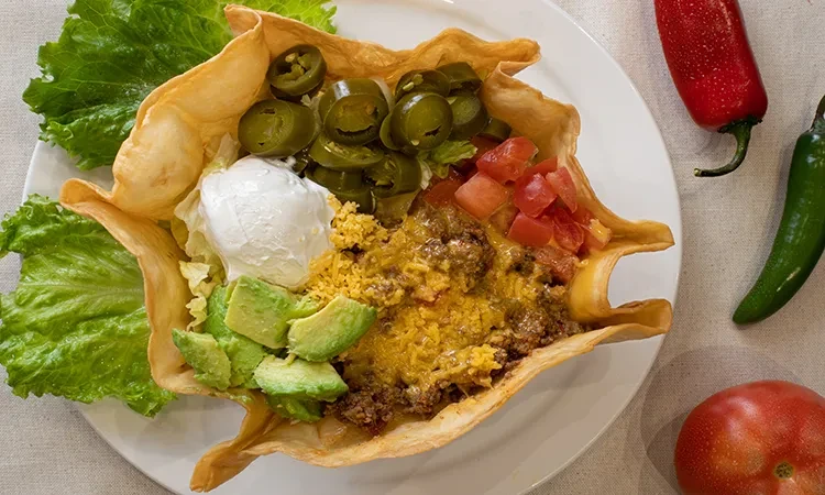 Taco salad in an edible tortilla bowl with fresh ingredients.