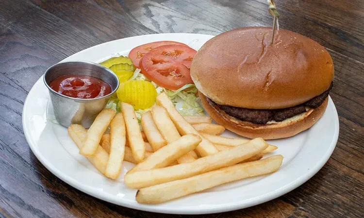 Cheeseburger with fries, ketchup, tomato, and pickles on a wooden table.