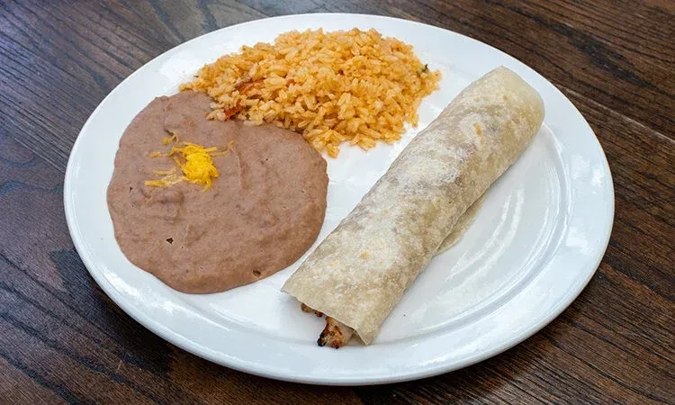 Burrito, refried beans, and Spanish rice on a wooden table.