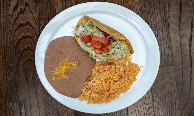 Hard-shell taco meal with beans and rice on a wooden table.