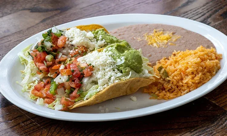Hard-shell taco, rice, and beans on a white plate.
