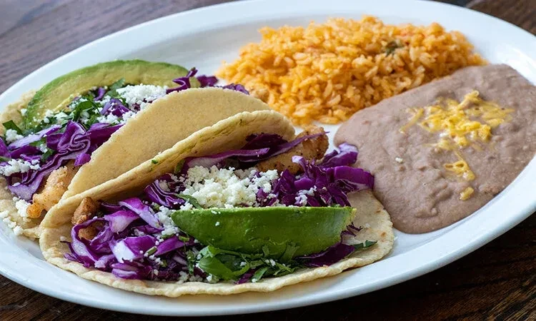 Two tacos with cabbage, cheese, cilantro, avocado; rice and beans.