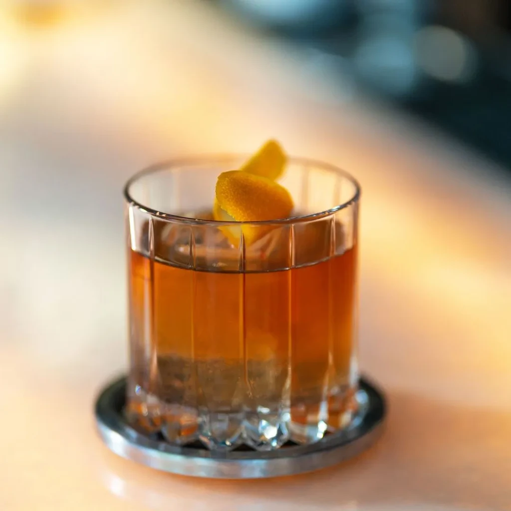 Amber cocktail in a rocks glass, garnished with two orange peels.