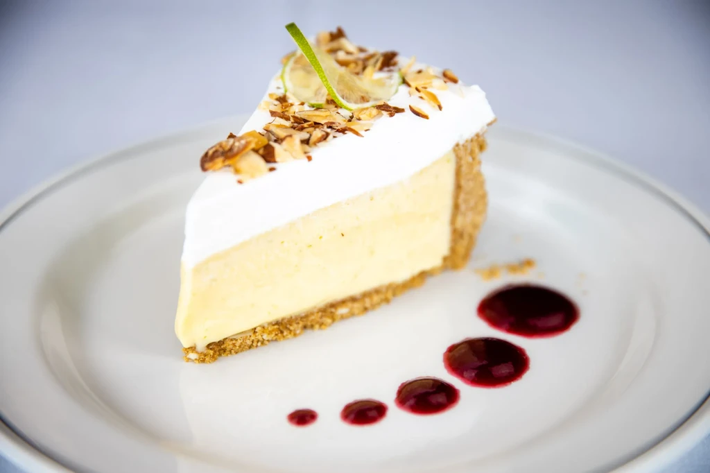 Slice of key lime pie with whipped topping and berry drizzle.