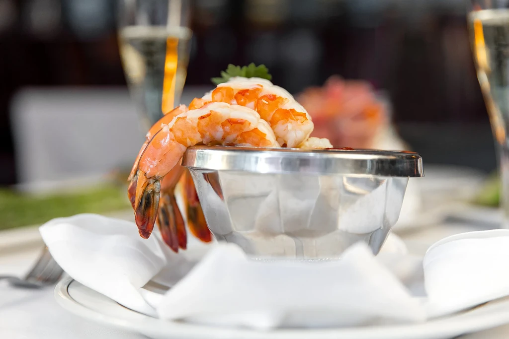 Shrimp cocktail in a silver bowl with a garnish of green herbs.