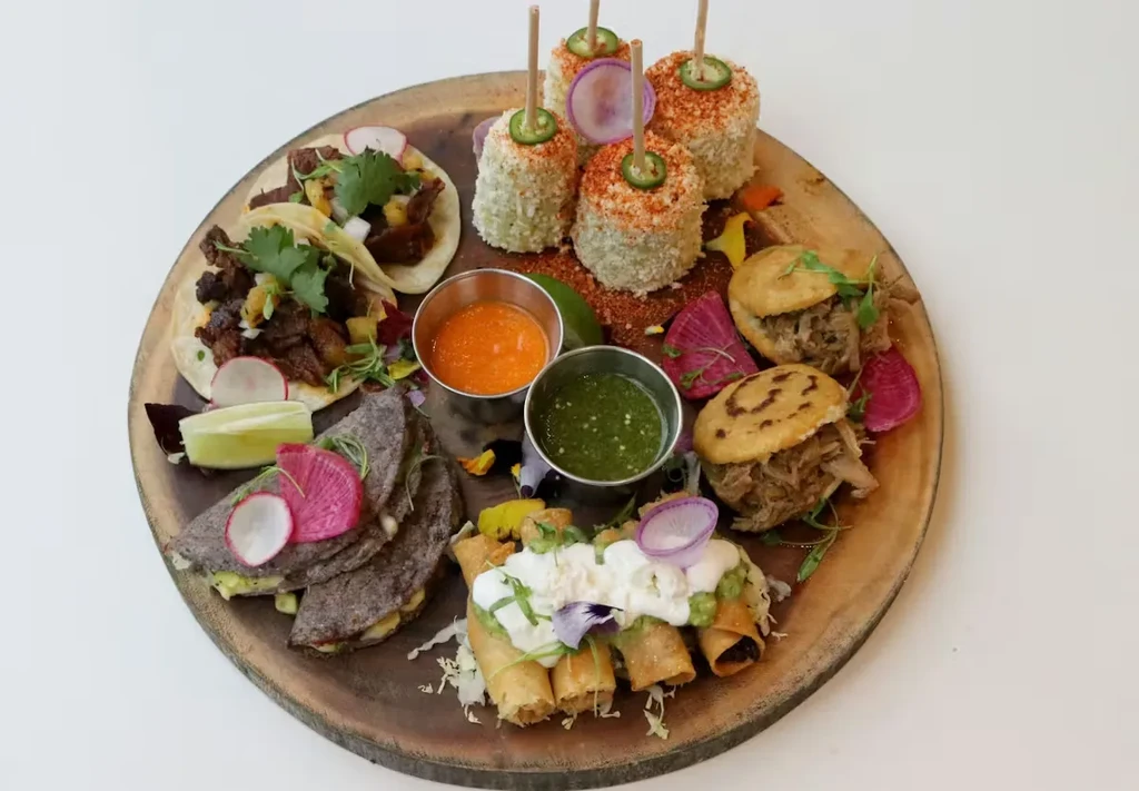 Wooden board laden with tacos, quesadillas, elotes, and other Mexican food.