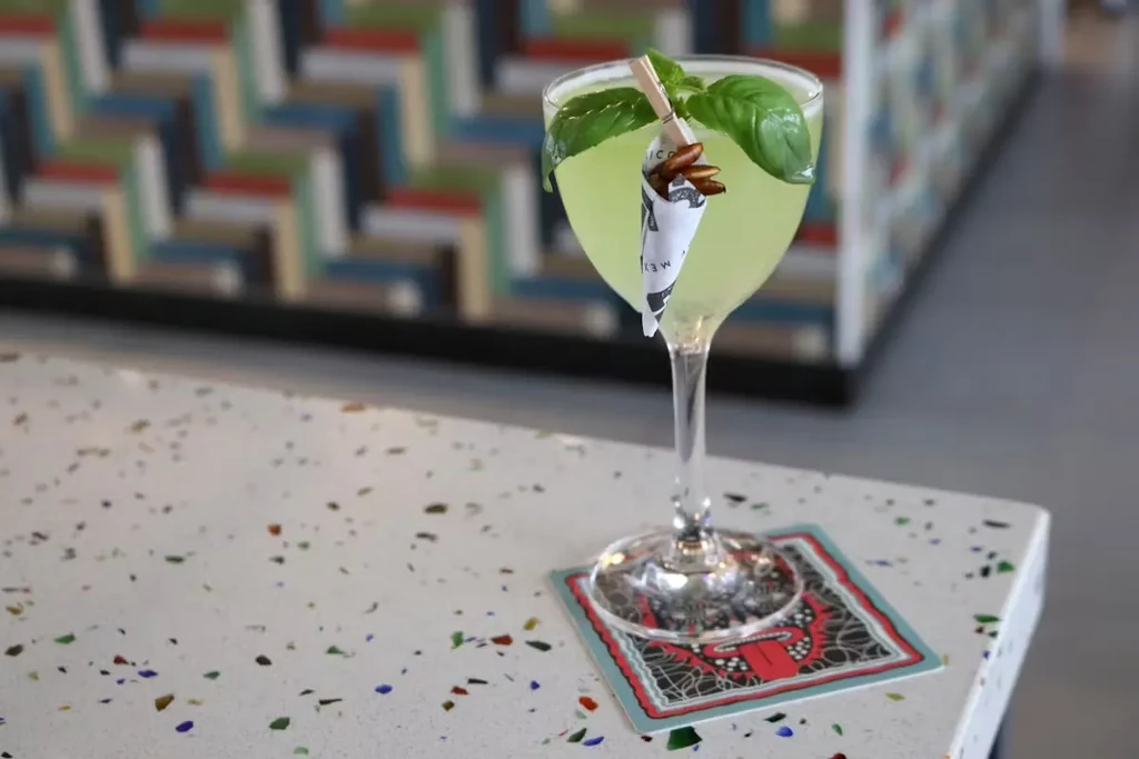 Green cocktail in coupe glass with basil leaves and nuts.
