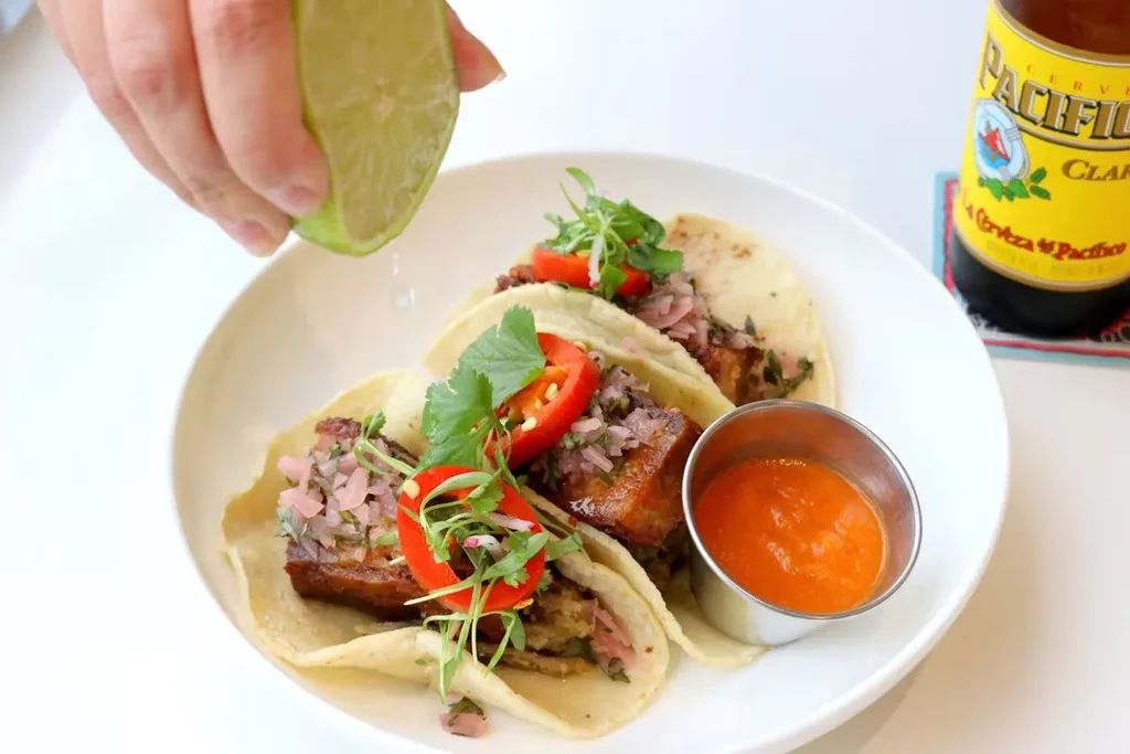 Three tacos with meat, salsa, cilantro, and lime on a white plate.