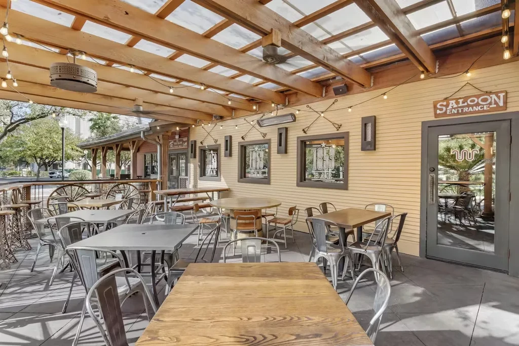 Outdoor patio with tables, chairs, pergola, and "1853 BAR" windows.