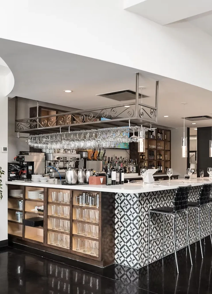 Well-stocked modern bar with espresso machine, bottles, and patterned tiles.