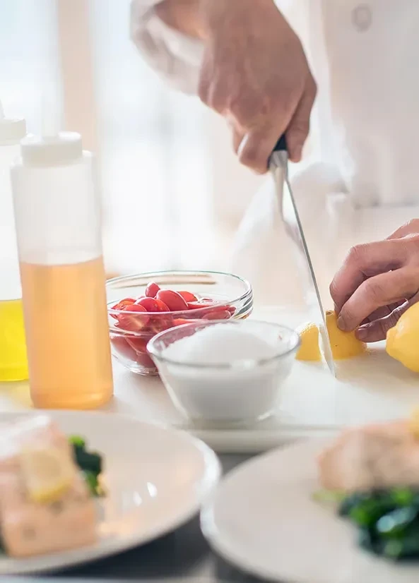 Chef's hands slice a lemon on a cutting board.