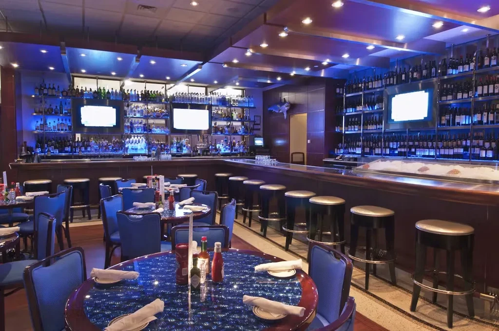 Well-stocked bar and dining tables with blue lighting in a restaurant.
