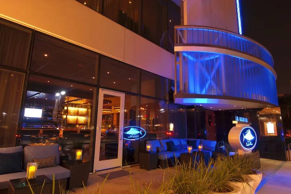Night view of Spilla restaurant exterior with fish sign and patio.