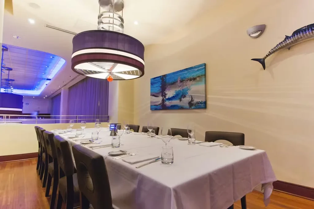 Empty dining table with chairs, purple chandelier, and marlin sculpture.