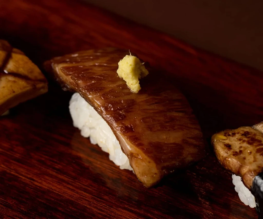 Close-up of nigiri sushi with seared meat and light yellow condiment.