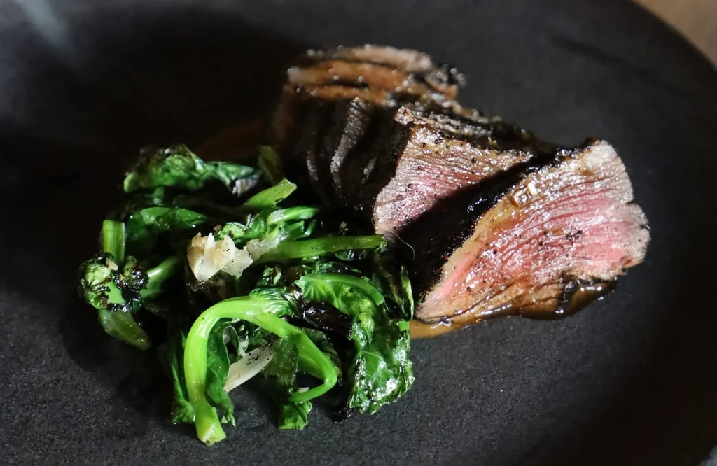 Sliced medium-rare steak with seared crust and green leafy vegetables.