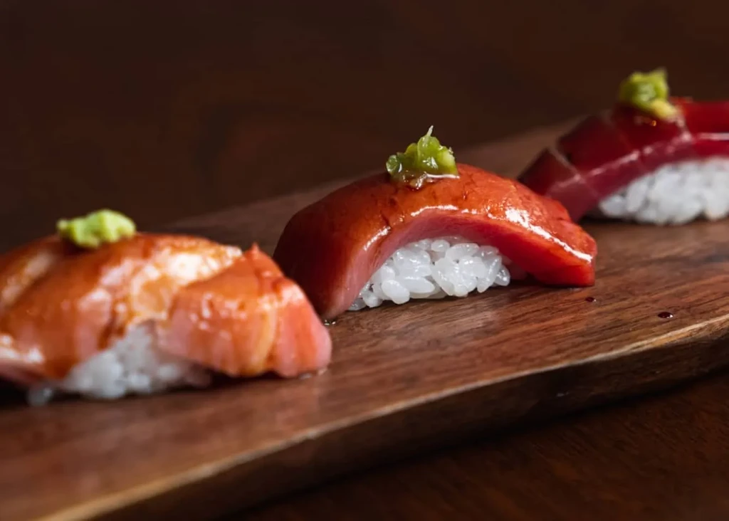 Three nigiri sushi pieces with fish and wasabi on a wooden board.