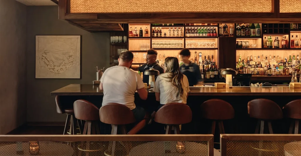 Stylish bar interior with bartenders, patrons, and liquor display.