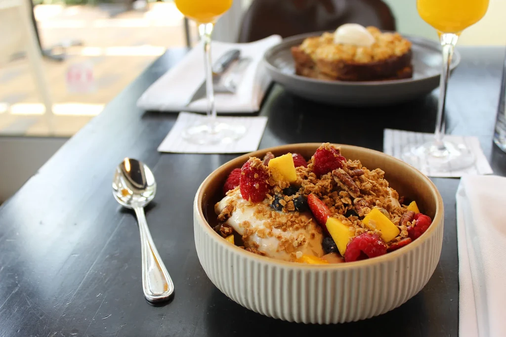 Bowl of yogurt with fruit and granola, drinks in background.