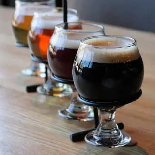 A flight of four beer samples, dark to light, on a wooden table.