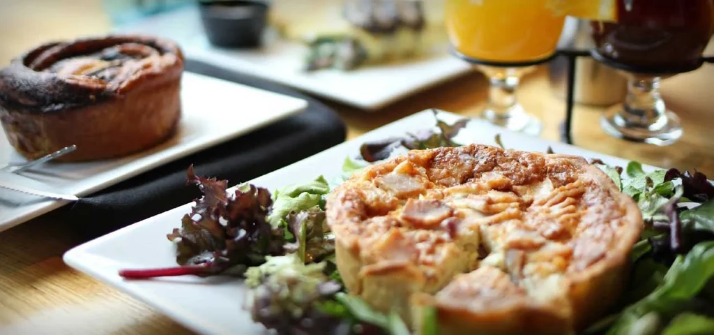 Close-up of a quiche, pastry, and two drinks on a wooden table.