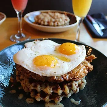 Chicken and waffles topped with two sunny-side-up eggs.