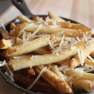 Golden french fries in a cast-iron skillet with shredded white cheese.