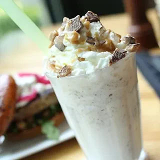 Creamy milkshake with whipped cream, caramel, chocolate, and green straw.