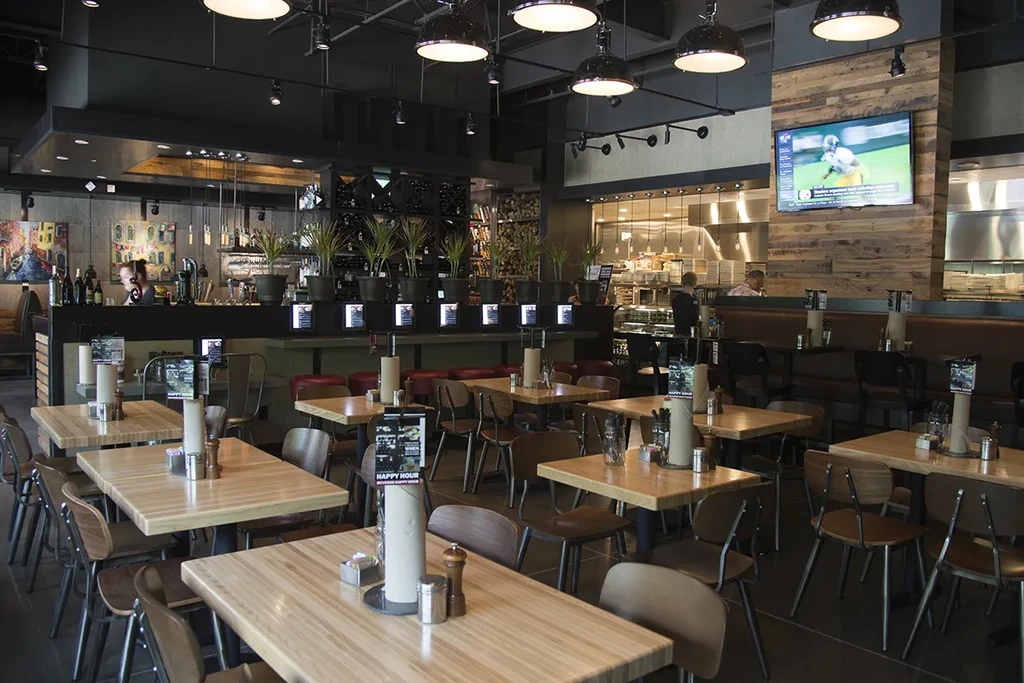 Contemporary casual restaurant interior: dining, bar, open kitchen, Happy Hour signs.
