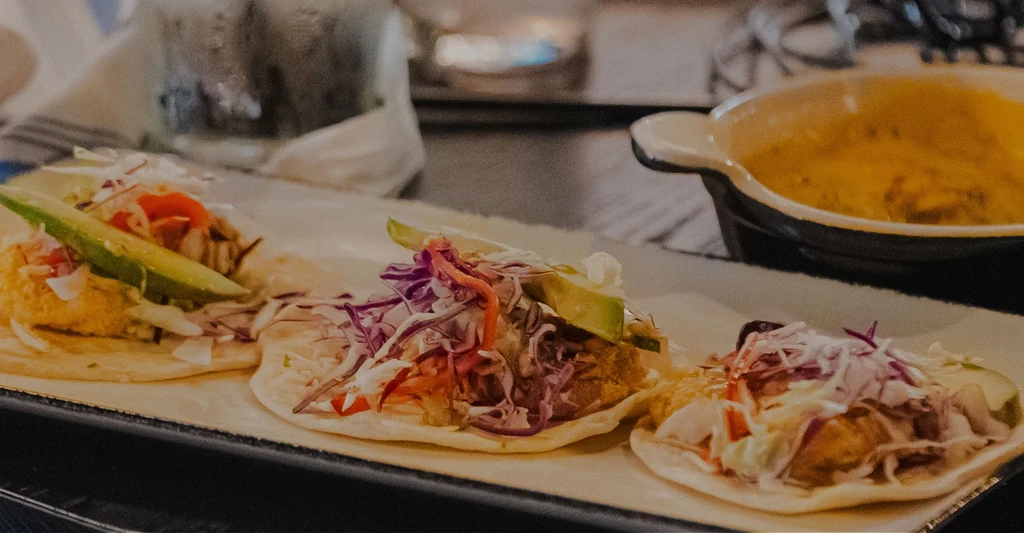 Three tacos with fish, slaw, and avocado on a rectangular plate.