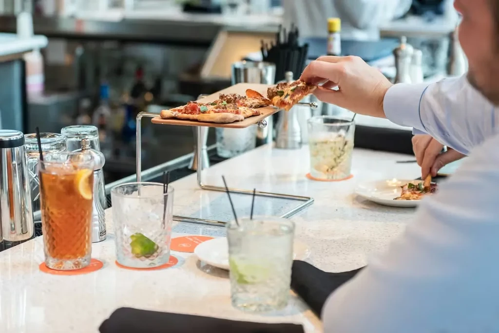 Hand taking slice of rectangular pizza from elevated stand.