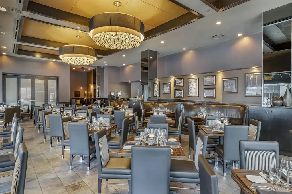Empty upscale restaurant dining room with set tables, booths, and chandeliers.