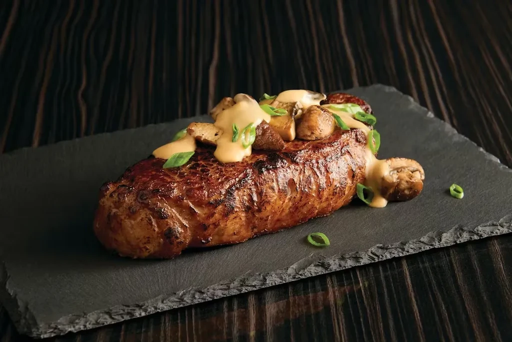 Grilled steak with mushrooms, creamy sauce, and herbs on a slate plate.