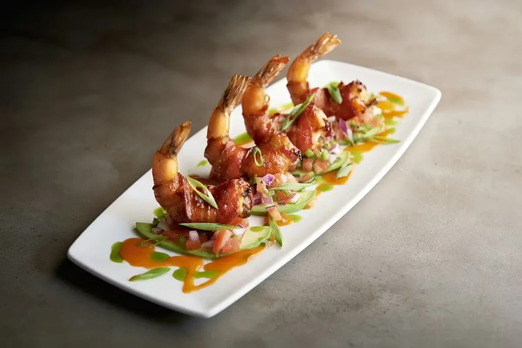 Three bacon-wrapped shrimp, avocado salsa, green and orange sauces.